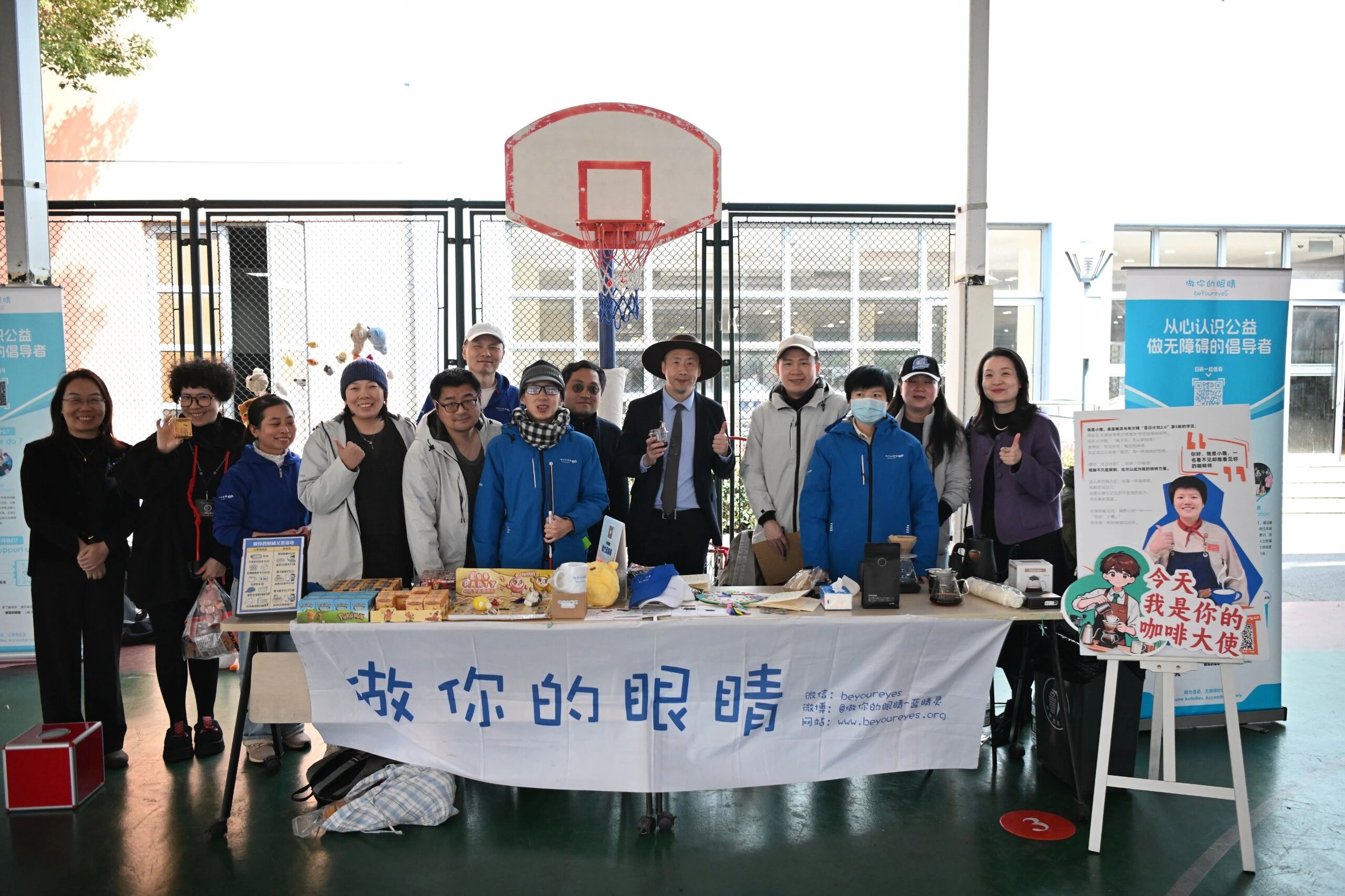 万源协和学校义卖活动的参与者在蓝睛灵展位前合影 Participants of the Wanyuan Xiehe School charity bazaar posing for a group photo in front of the Lanjingling booth